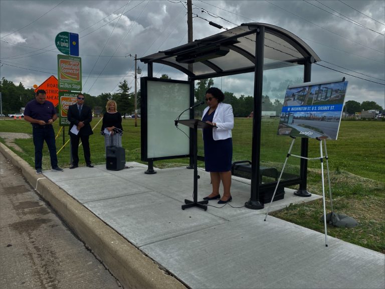 Woman speaks at a podium near a bus stop