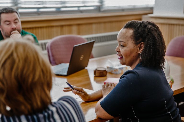 an employee speaks to two employees at a table