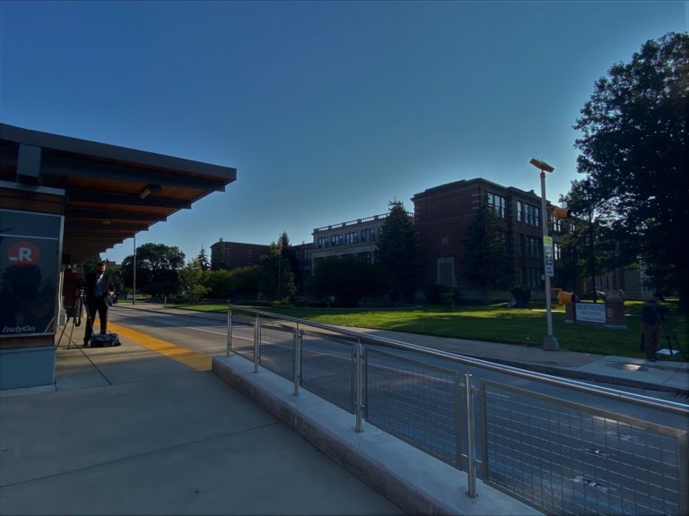 man standing at bus station outside Shortridge High School